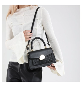 Détail du sac à main noir motif crocodile avec fermoir doré porté par le mannequin