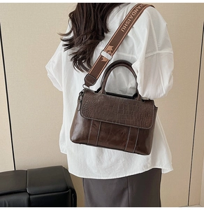 Detail of dark brown leather tote with crocodile texture flap and woven strap detail