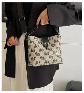 Detail of ARCK print on beige woven bucket bag with black leather handle and strap