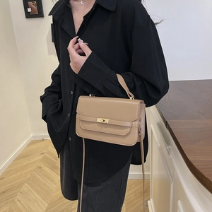 Khaki leather crossbody bag with top handle and gold metal twist lock on black shirt
