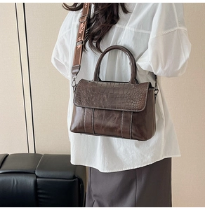 Detail of dark brown tote bag with crocodile texture flap and wide logo fabric strap