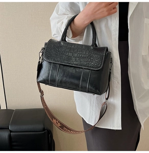 Detail of crocodile embossed leather handbag with contrast stitching and woven logo strap