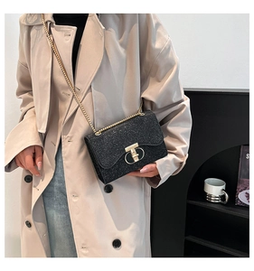 Détail du sac bandoulière noir pailleté avec chaîne dorée porté sur un manteau