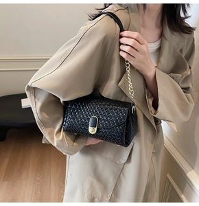 Détail du sac à bandoulière tressé noir avec chaîne dorée et fermoir pivotant en métal