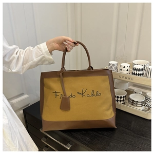 Detail of a mustard yellow tote bag with brown leather trim and Frida Kahlo signature