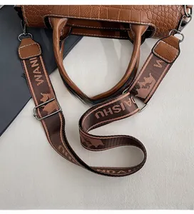 Dettaglio della tracolla larga in tessuto regolabile con ganci metallici su borsa marrone