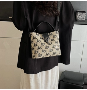 Detail view of beige printed canvas bucket bag with black leather strap on model