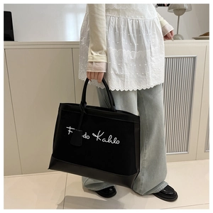 Detail of black canvas tote bag with Frida Kahlo lettering and leather handles