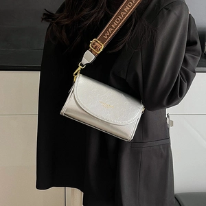 Silver leather crossbody bag with wide printed shoulder strap on a black blazer