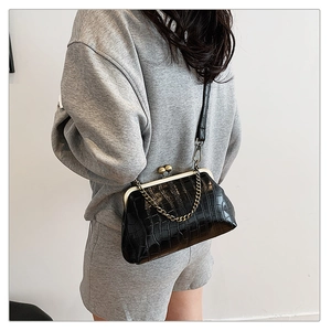 Detail of black crocodile texture bag with gold kiss-lock closure and metal chain strap