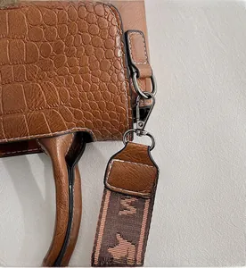 Dettaglio della borsa in pelle a coccodrillo con ganci metallici e tracolla intrecciata