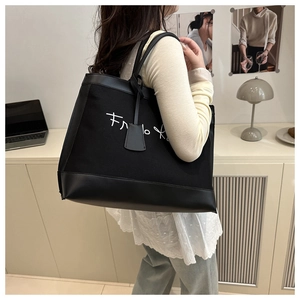 Detail of black canvas tote bag with leather bottom and artistic white script lettering