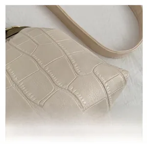Close-up of cream faux leather shoulder bag with embossed stone texture and strap
