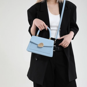 Sac à main bleu en simili crocodile avec fermoir doré porté par un modèle en costume noir
