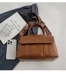 Dettaglio della borsa marrone in pelle a coccodrillo con ampia tracolla in tela