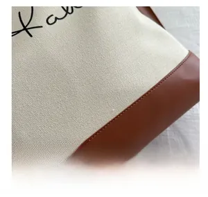 Close-up of canvas and brown leather stitching with detailed embroidery on a tote bag