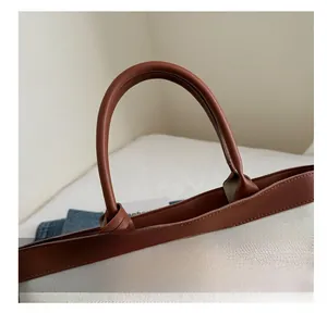 Detail of round brown leather handles and beige canvas texture on the tote bag