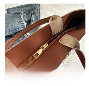 Close-up of smooth gold metal zipper on brown leather and canvas tote bag