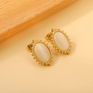 Detailed side view of oval gold stud earrings with white cat eye stone and sunburst texture