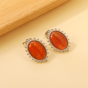 Detailed shot of oval orange cat-eye stud earrings with silver beaded edges on wood
