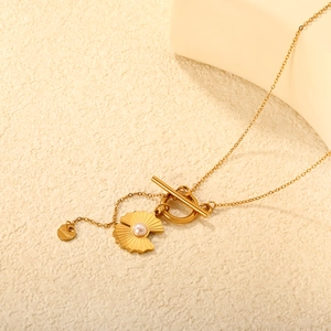 Detail of gold stainless steel shell pendant with pearl and OT buckle on neutral background