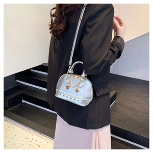 Detail of silver metallic shell bag with gold dice charm and stud accents shown on model
