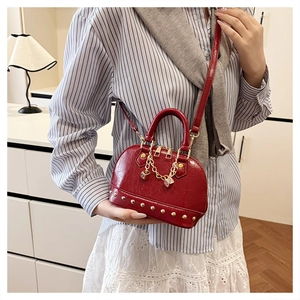 Detail of red shell handbag with gold rivets and dice charm worn by model in room
