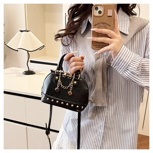 Detailed view of black leather shell bag with gold studs and dice chain accessory