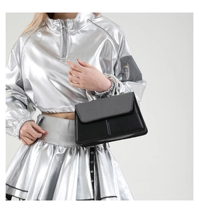 Detail of a chic black textured handbag featuring a circular silver metal handle