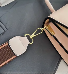 Close-up of golden hardware hook and pink leather stitching on a stylish crossbody bag