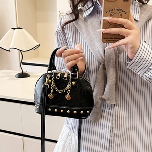 Elegant black shell handbag with golden studs and dice chain worn on a striped shirt