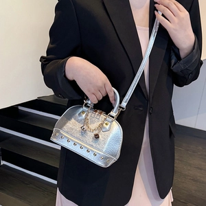 Silver studded shell bag with gold chain charm on a model in a modern interior