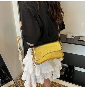 Detailed view of a gold snakeskin textured crossbody bag worn on a model's shoulder
