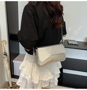 Detail of silver snake-pattern crossbody bag worn on shoulder with metallic finish texture