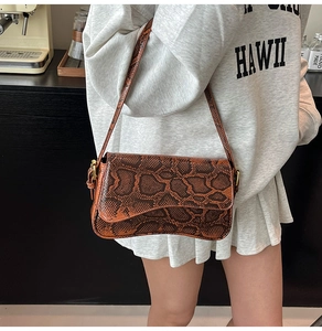 Detail of dark brown snakeskin texture with gold hardware on a curved crossbody bag