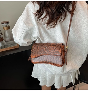 Detail of brown snake print faux leather crossbody bag with gold hardware and curved base