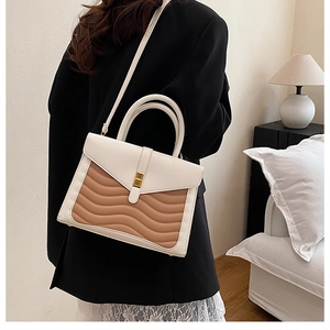 Detail of wave-patterned stitching and metal buckle on a two-tone crossbody handbag