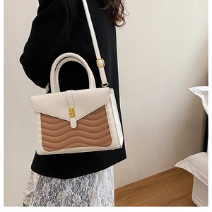 Detail of wavy textured stitching and golden metal clasp on bicolor crossbody handbag