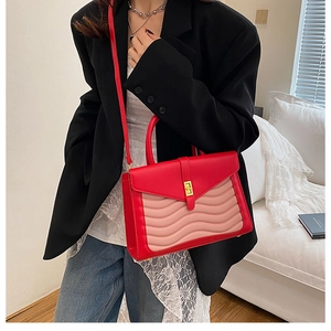 Detail shot of a red and pink contrast shoulder bag with golden twist lock on a model