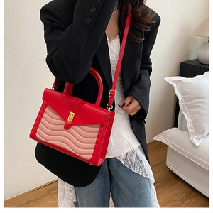 Detailed view of red and pink crocodile texture handbag with gold metal clasp on model