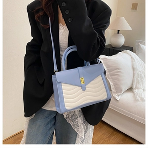 Detail of blue and beige paneled handbag with wavy quilting on a model in a home setting