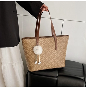 Close-up of brown patterned tote bag featuring letter prints and a white pompom charm