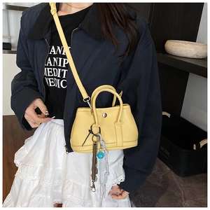 Détail du sac seau jaune en cuir grainé avec breloque tressée et décor en ressort