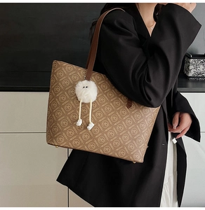 Close-up of brown tote bag with letter print and cute white plush monster charm detail