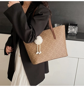 Detail view of large brown leather tote bag with letter prints and white pompom charm