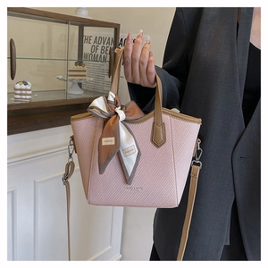 Détail du sac seau rose tissé avec poignées en cuir marron et foulard en soie décoratif