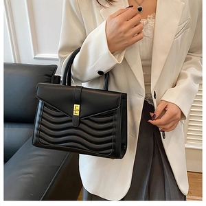 Close-up of wavy quilted pattern and gold metal clasp on a black luxury handbag