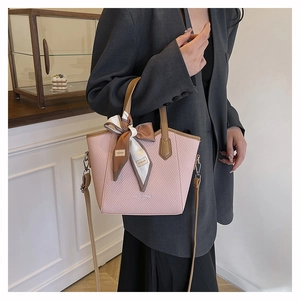 Détail d'un sac seau rose tressé avec des poignées en cuir marron et un foulard de mode