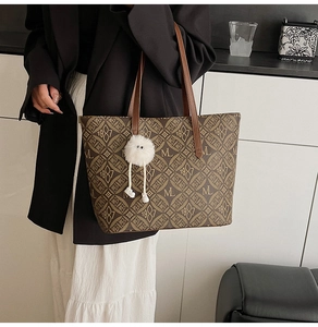 Detail of vintage tote bag featuring brown letter monogram and white fuzzy pom-pom charm