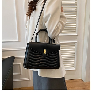 Detail of black wave quilted handbag featuring gold turn-lock clasp and slim strap